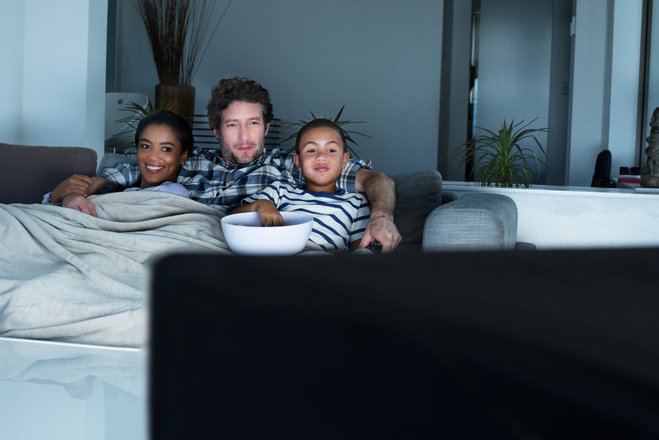 duas crianças e um homem assistindo tv na cama