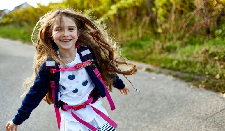 Menina sorridente correndo em dire&ccedil;&atilde;o &agrave; c&acirc;mera com mochila nas costas.