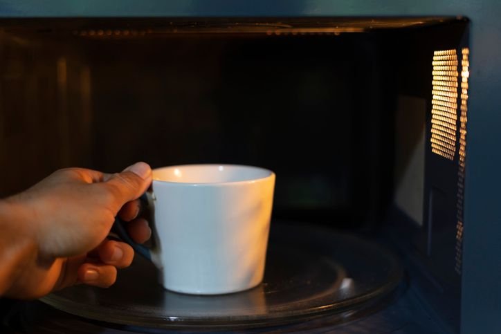 mão colocando uma caneca branca dentro do microondas