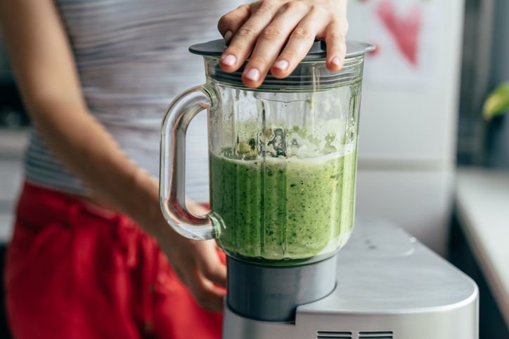 Pessoa preparando um smoothie verde em um liquidificador da promo&ccedil;&atilde;o em uma cozinha moderna, ideal pra quem busca op&ccedil;&otilde;es saud&aacute;veis e nutritivas.