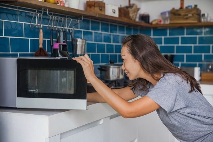 mulher usando o micrrondas na bancada da cozinha