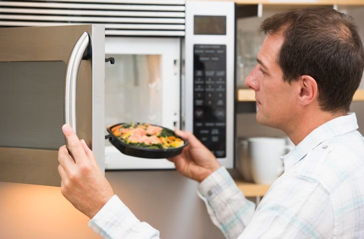 Homem inserindo marmita no micro-ondas em cozinha doméstica
