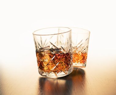 Dois copos de whisky ou bourbon com gelo, servidos em fundo escuro para comparar as bebidas.