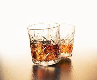 Dois copos de whisky ou bourbon com gelo, servidos em fundo escuro para comparar as bebidas.