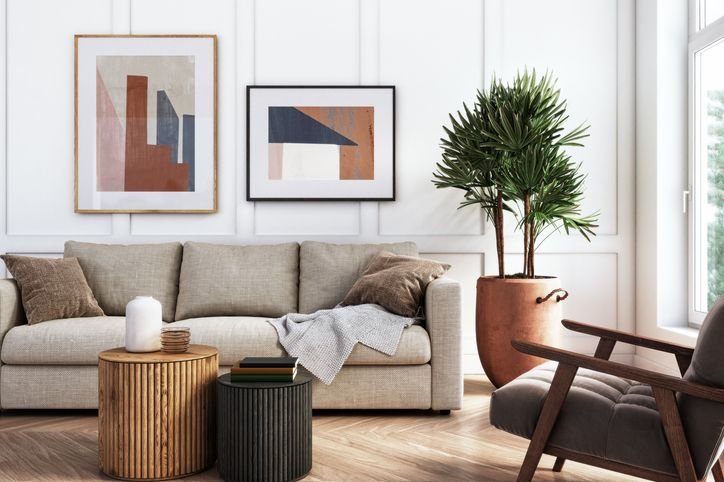 Sala de estar com sof&aacute; moderno e decorada com quadros abstratos, planta grande e mesas de centro elegantes, ideal pra um ambiente contempor&acirc;neo.