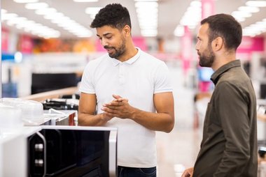 Cliente e vendedor em loja de eletrodomésticos consultando especificações de micro-ondas juntos