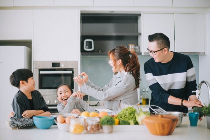  Fam&iacute;lia jovem com dois filhos preparando comida juntos em cozinha moderna com forno embutido ao fundo