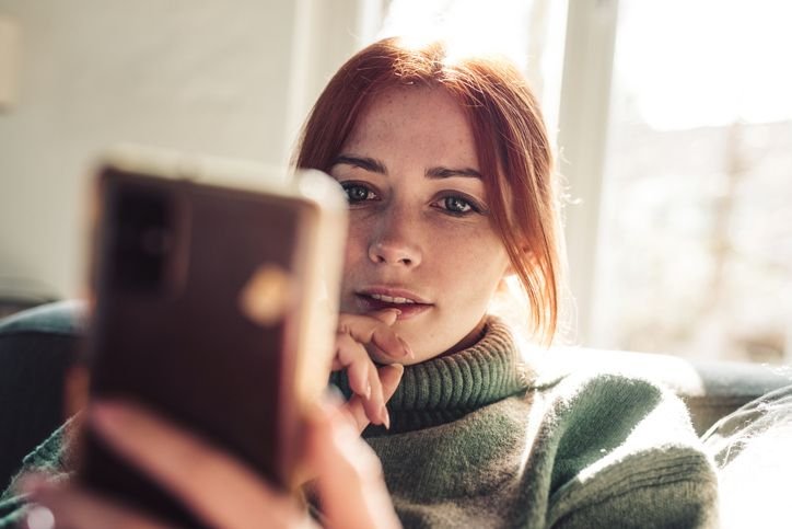 Mulher segurando celular e olhando para a tela.