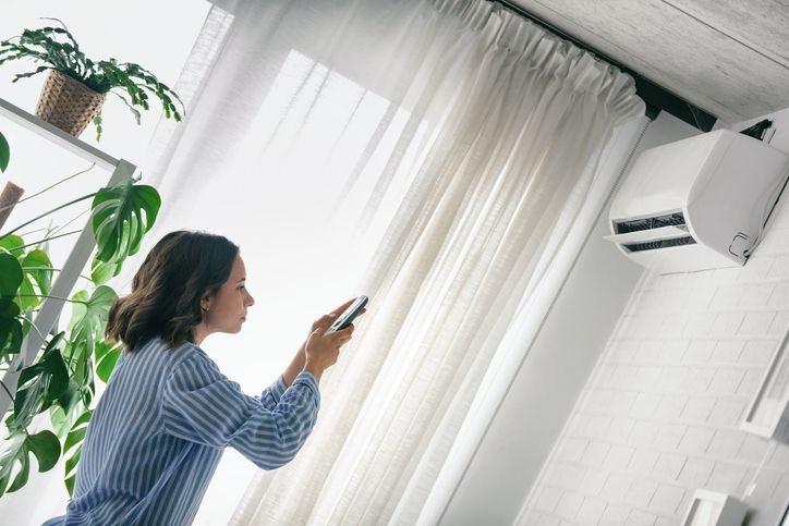 Mulher em casa usando controle remoto pra ajustar o ar condicionado inverter em ambiente residencial moderno.