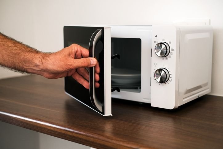 Mão abrindo porta de micro-ondas na cozinha