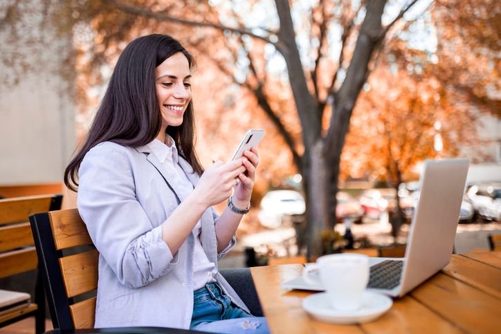 Jovem usando smartphone ao ar livre em uma cena urbana, com foco no uso do celular pra mensagens, redes sociais e rotina digital.