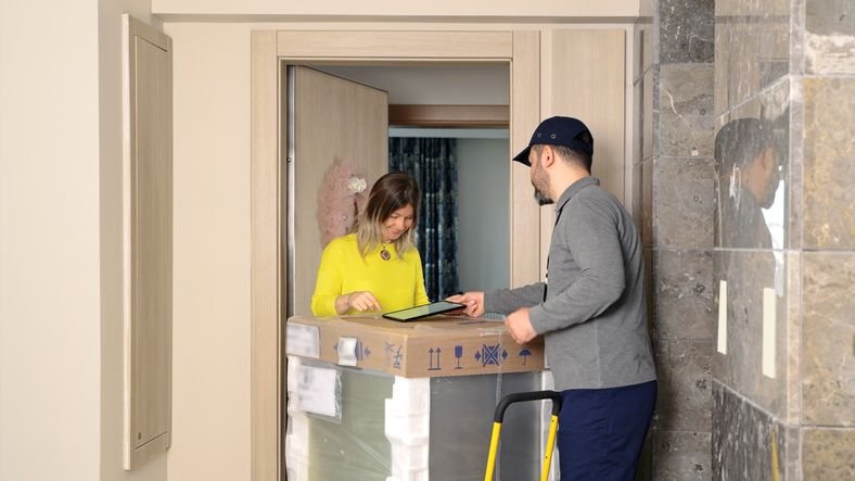 Entrega de um aparelho de lava e seca Hisense por um entregador a uma mulher em um ambiente residencial, destacando a facilidade de compra e instala&ccedil;&atilde;o do eletrodom&eacute;stico.  