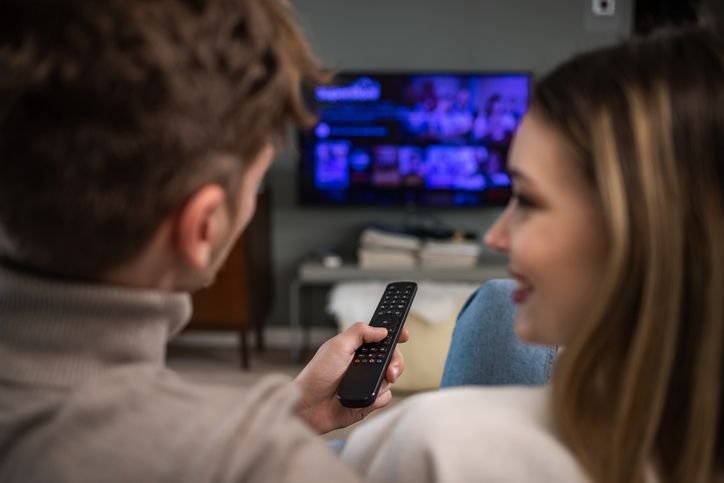  casal sentado na sala e escolhendo um filme confortavelmente na sua smart TV 4K