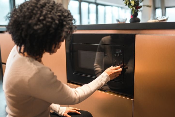  Mulher usando um micro-ondas embutido em nicho planejado na cozinha.