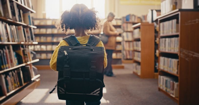 Menina de costas com mochila preta em uma biblioteca