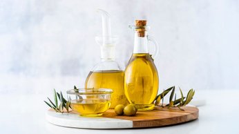 Garrafas de vidro com azeite sobre uma tábua, representando o que é galheteiro e como usar temperos na cozinha.