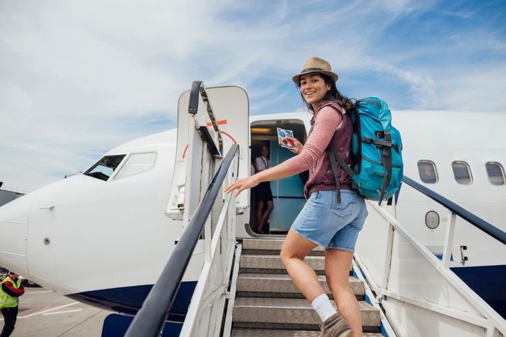 Mulher em pé com mochila de viagem nas costas subindo a escada do avião.