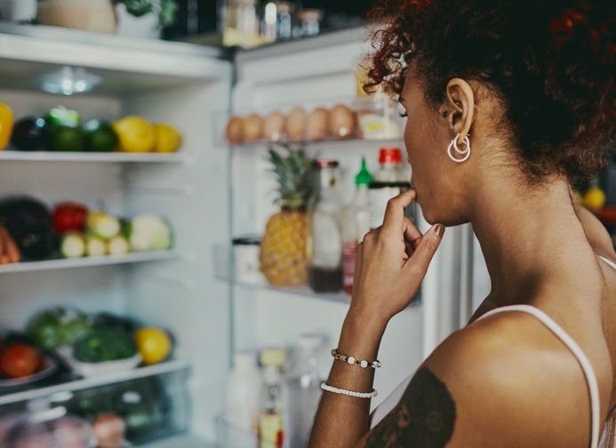 Mulher com m&atilde;o ao queixo, escolhendo alimentos, representando bem-estar ao acertar na escolha da geladeira.