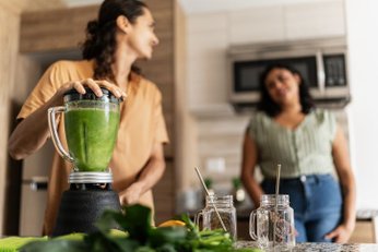 Duas mulheres na cozinha, o foco é um liquidificador com batida verde dentro