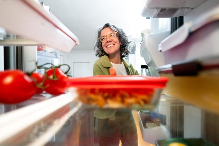 Mulher escolhendo alimentos no interior da geladeira, ilustrando dicas de como escolher uma geladeira ideal para sua casa.