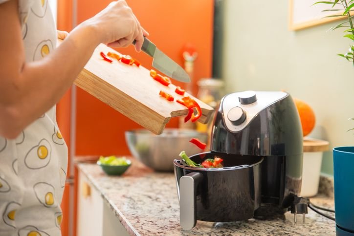 pessoa colocando legumes no cesto de uma air fryer EOS pra ass&aacute;-los sem &oacute;leo. 