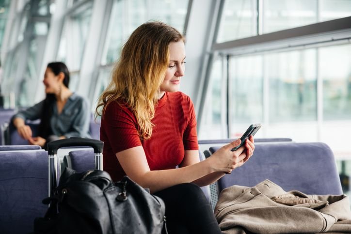 Mulher de roupa vermelha usando smartphone Poco C75 enquanto aguarda em ambiente externo com luz natural.