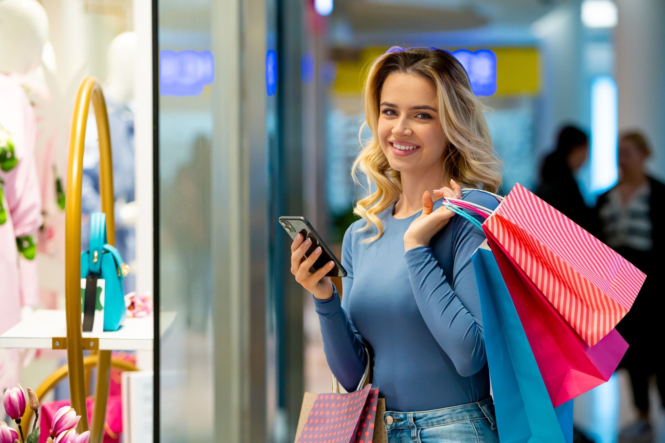 Mulher sorridente aproveitando ofertas em uma loja durante a liquida&ccedil;&atilde;o fant&aacute;stica Magalu, com roupas e acess&oacute;rios ao fundo.