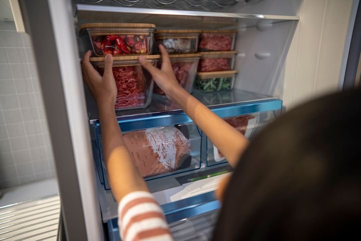 Mulher colocando marmitas na geladeira, bem organizada e espaçosa.