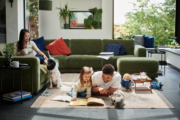 Família em sala aconchegante com sofá verde musgo, plantas e luz natural, mostrando um ambiente confortável para descanso e convivência.