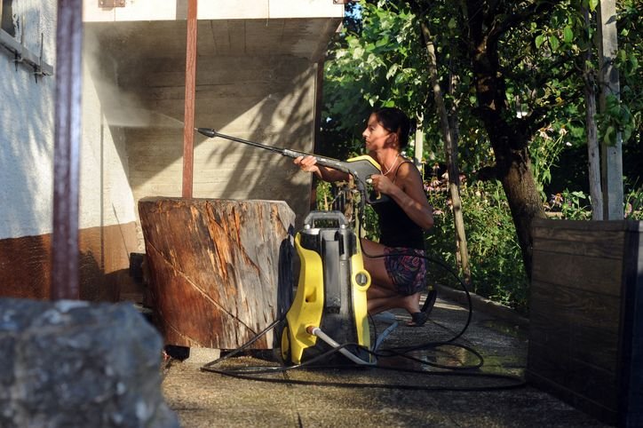 Mulher utilizando lavadora de alta press&atilde;o pra limpar parede externa em &aacute;rea residencial, removendo sujeira com jato de &aacute;gua e realizando limpeza dom&eacute;stica eficiente