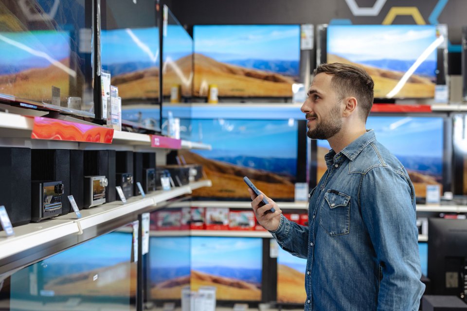 Homem comprando uma TV em promoção em loja de eletrônicos, sendo uma escolha ideal pra melhorar a sua experiência de entretenimento.