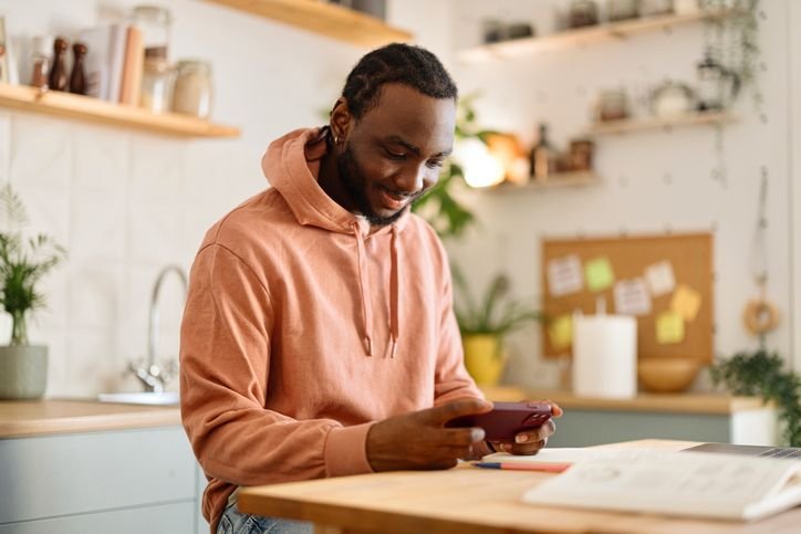 Jovem sentado em mesa usando smartphone Realme Note 50 com expressão concentrada e foco na tela.