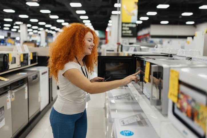 Mulher examinando um micro-ondas em loja de eletrodomésticos.