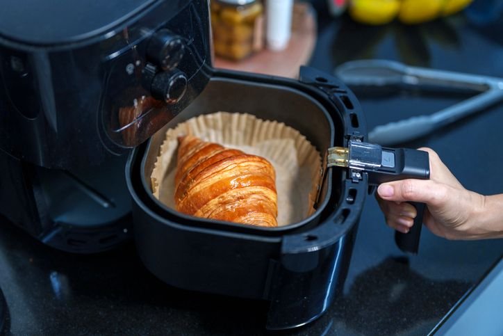 Mulher retirando croissant de chocolate da fritadeira a ar com pegador, mostrando que a air fryer Gaabor é boa. 