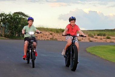 Dois adolescentes andando de bicicleta elétrica na rua.