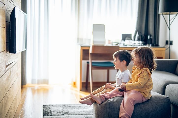 crianças sentadas em uma almofada assistindo à TV 28 polegadas pendurada na parede em um home office