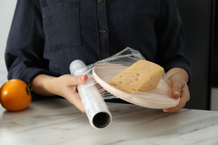 M&atilde;os embalando com papel filme um queijo