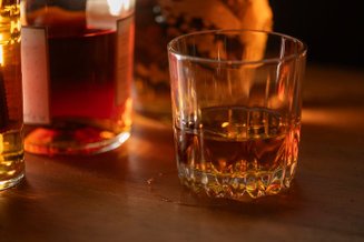 Copos de whisky sobre mesa de madeira, destacando a bebida feita a partir de cereais fermentados e envelhecidos.