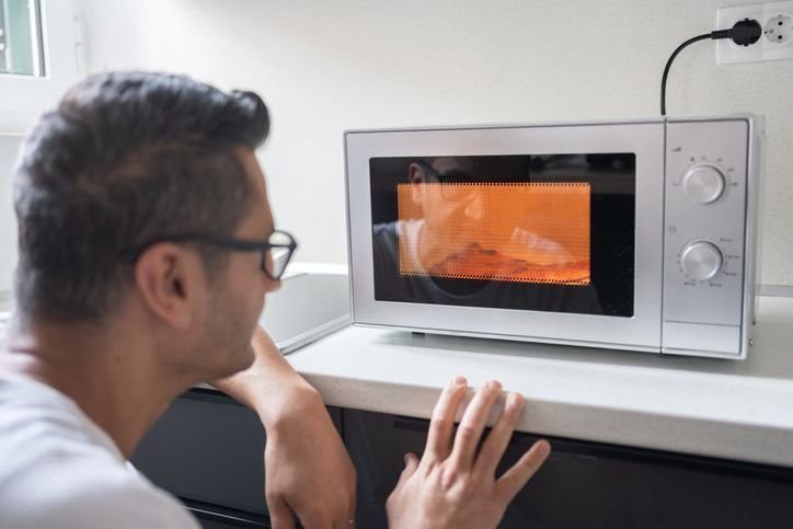 Homem de frente ao microondas esperando sua comida