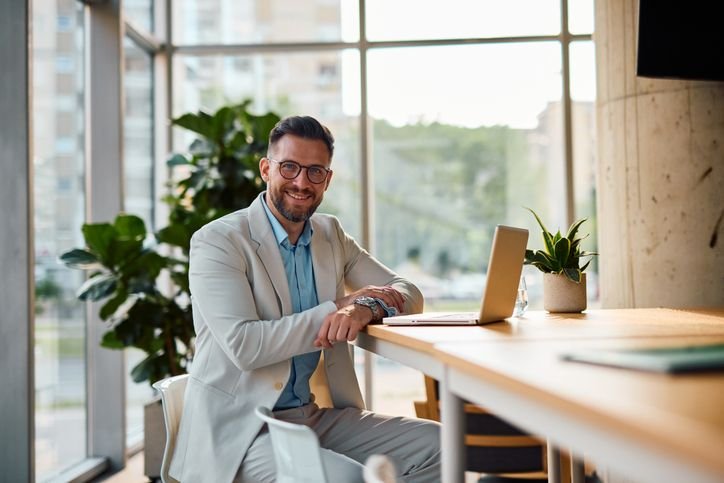 homem num escritório com terno branco em frente ao notebook