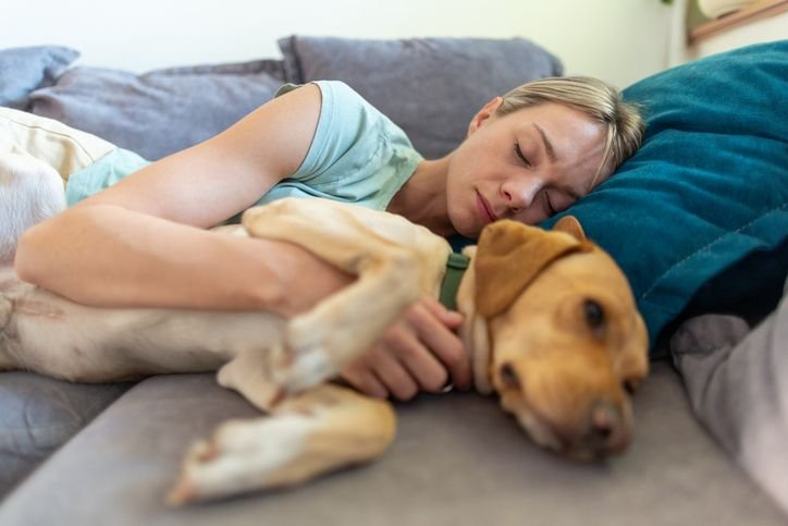Mulher cochilando em sofá-cama com seu cachorro.