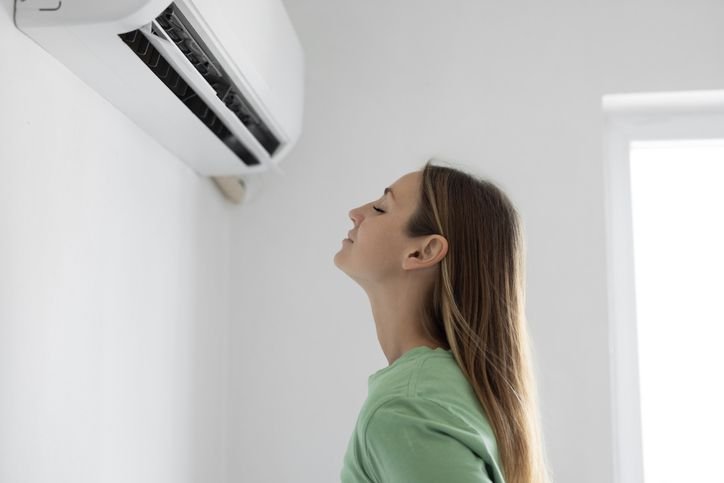 Imagem de uma mulher recebendo ar fresco do ar condicionado split instalado na parede, ideal pra manter ambientes frescos e confort&aacute;veis em resid&ecirc;ncias e escrit&oacute;rios.