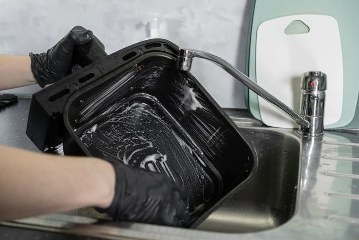 Pessoa limpando o cesto da air fryer, representando cuidados para escolher e manter uma air fryer que não enferruja.