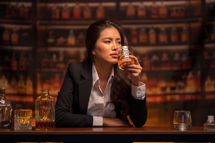 Mulher avaliando o aroma do whisky em uma ta&ccedil;a, cena ligada &agrave; an&aacute;lise de qualidade e autenticidade da bebida. 
