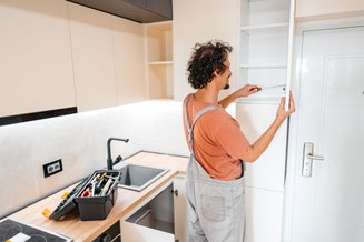 Homem de costas utilizando ferramenta para montar armários de cozinha.