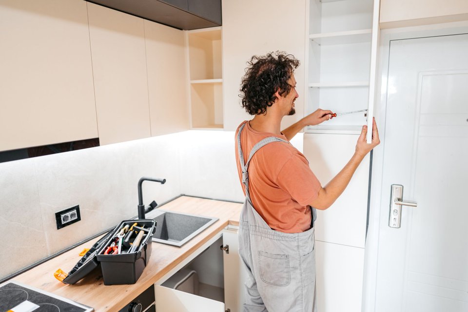Homem de costas utilizando ferramenta para montar armários de cozinha.