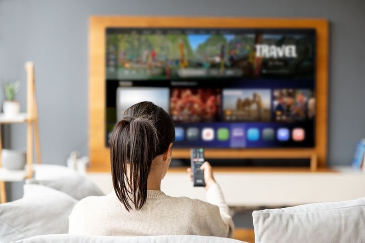 mulher sentada em um sofá de uma sala confortável usando o menu interativo da sua TV OLED 65