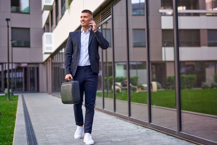  Homem de terno azul com tênis branco caminhando e falando ao celular, look masculino moderno que combina elegância e estilo casual.