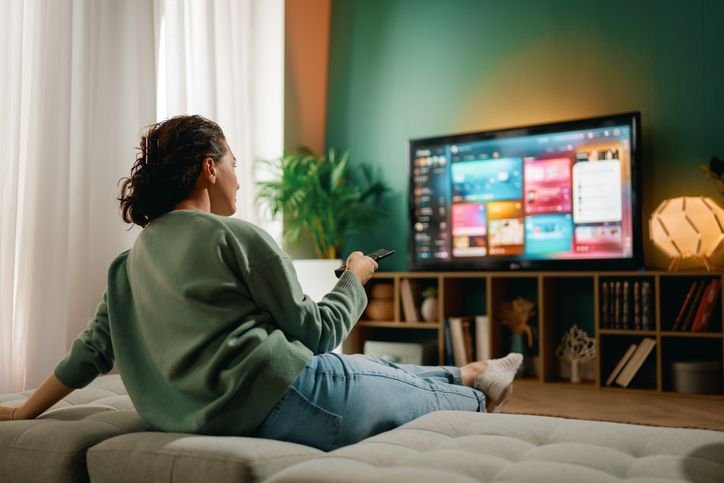 mulher em uma sala confortável sentada no sofá comendo pipoca e assistindo a um programa na sua TV LED acima da lareira acesa.