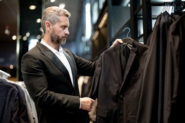 homem vestindo um terno preto está numa loja olhando outros ternos